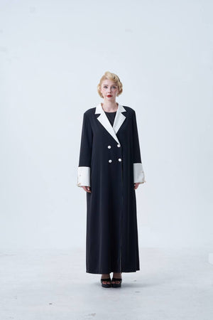 Person wearing a long black coat with white trim on a white background